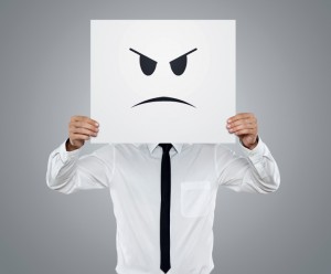 Young businessman holding card with a angry face on it