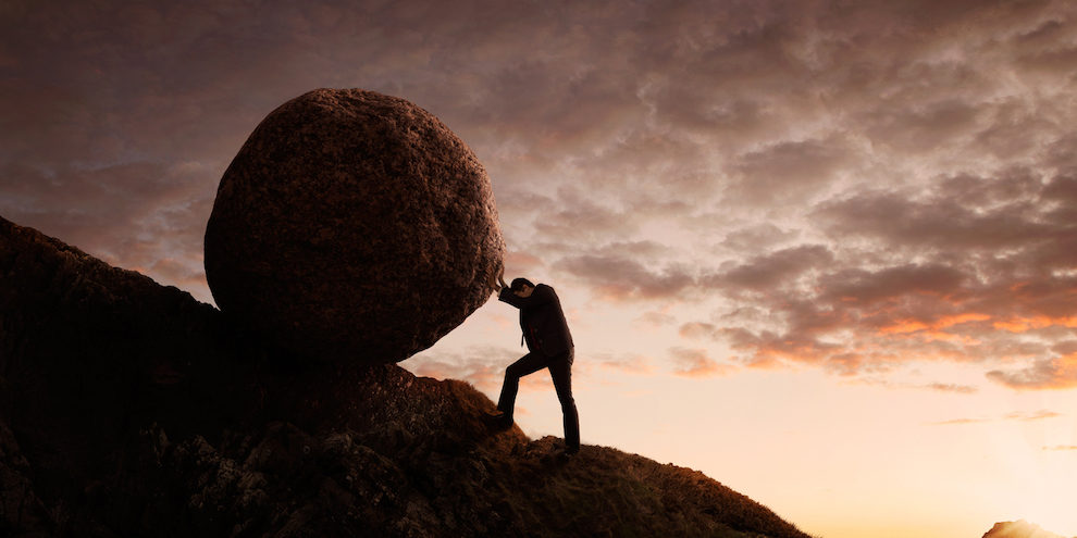 Business person pushing a boulder up a mountain.