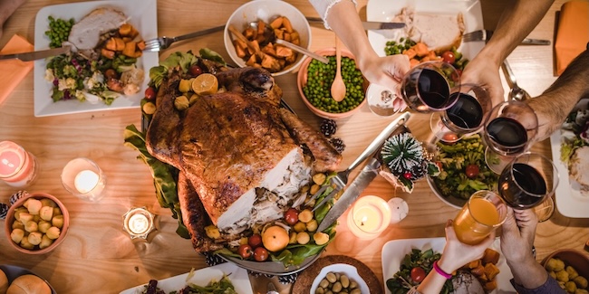 A Thanksgiving dinner table with turkey, dinner plates and people holding up their drinks.